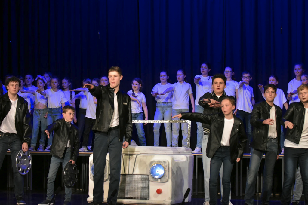 Cast performing around a mock car prop