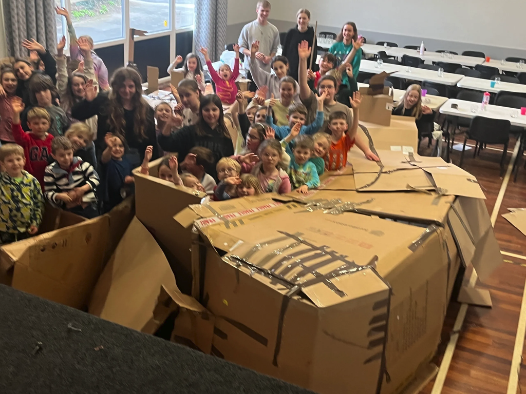 Two children peeking through a window cut into a cardboard den
